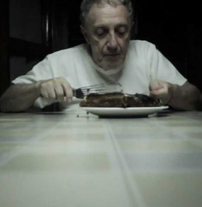 Un uomo anziano seduto a tavola mangia un dolce con una paletta da cucina